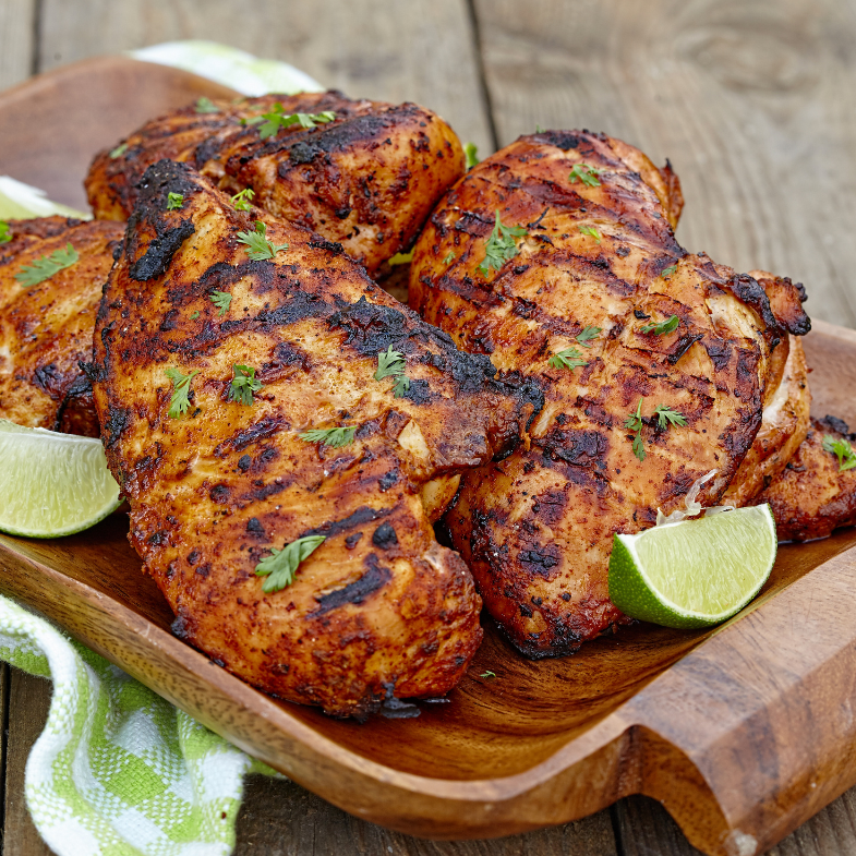 A picture of marinated and season chicken breasts on a wooden cutting board with slices of lime around it
